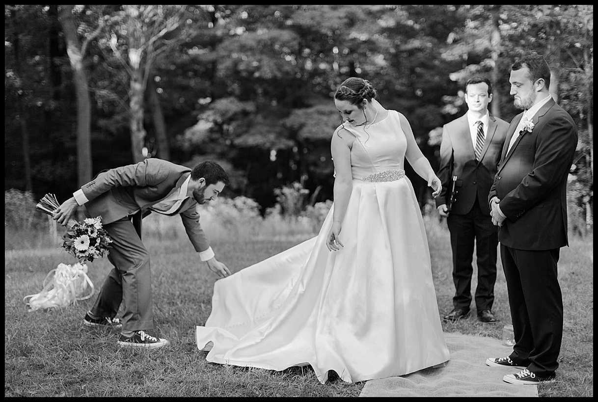 During an elopement ceremony in Hocking Hills state park in Ohio, the bride’s brother acts as man of honor and adjusts the bride’s wedding dress.