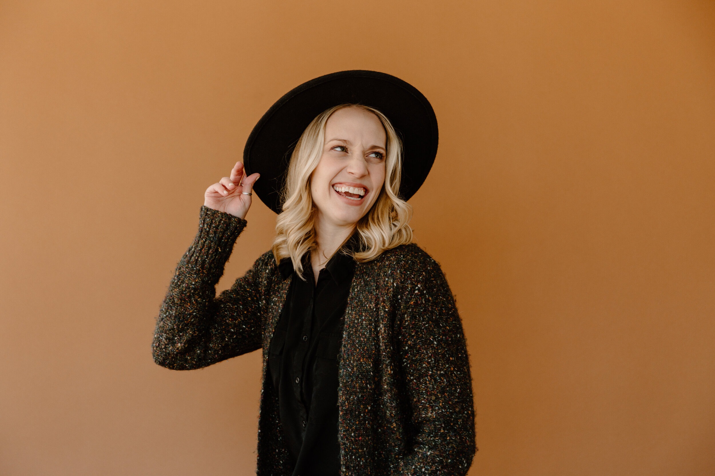 Photo from a branding shoot at West Studio in Ferndale, Michigan. Madison wore a wide-brimmed hat and cozy sweater to contrast the orange background.