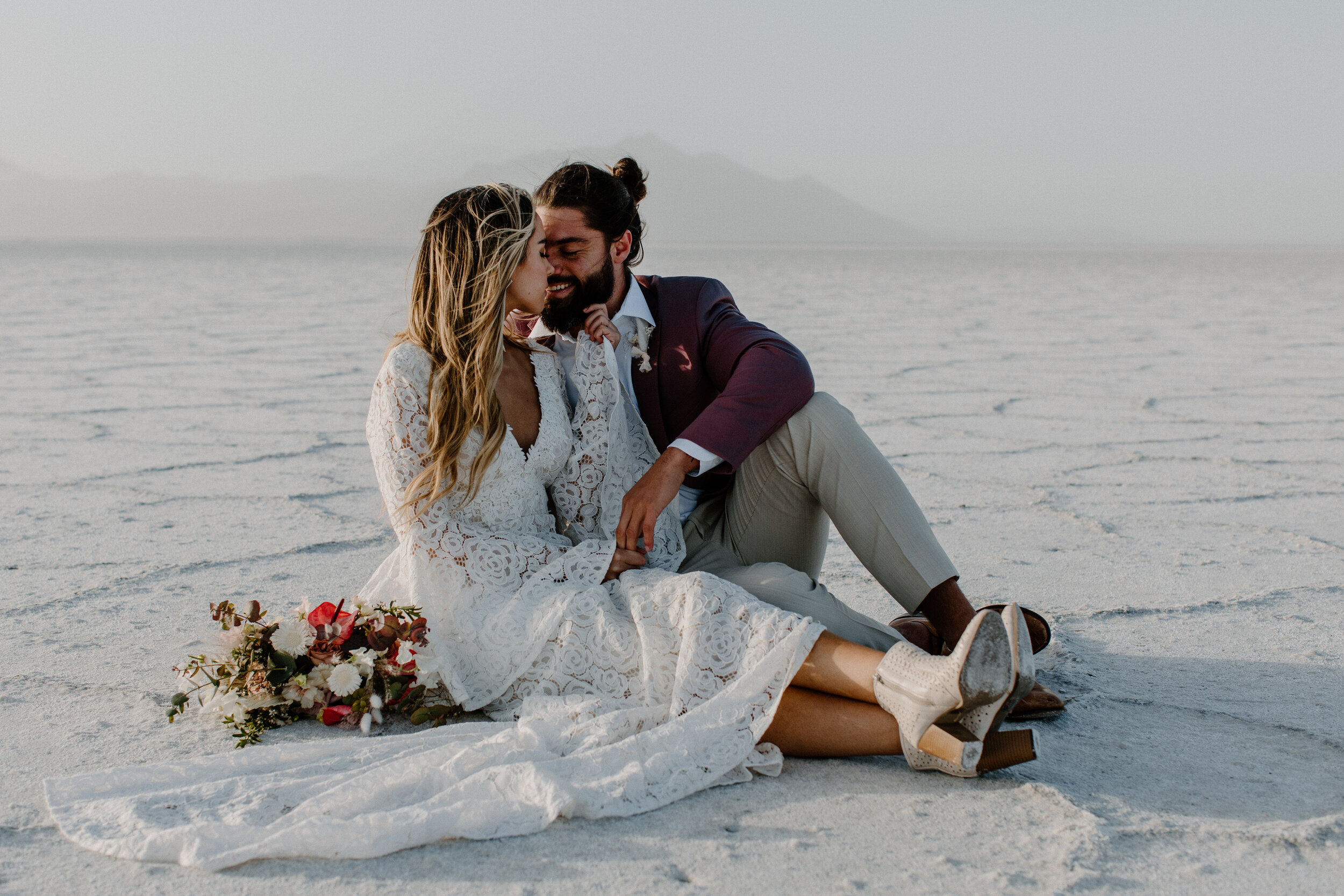 A destination wedding photoshoot in Booneville Salt Flats in Utah. The couple has a whimsical style, with the bride in a lace wedding dress and groom in a dusty pink suit.