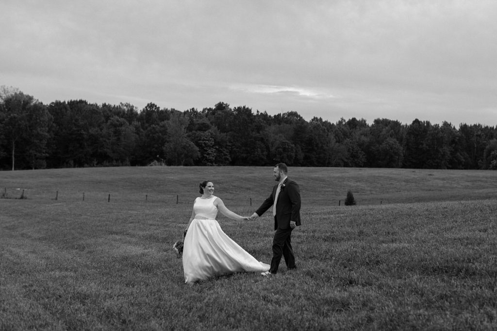 bride and groom holding hands walking alone through a large pasture