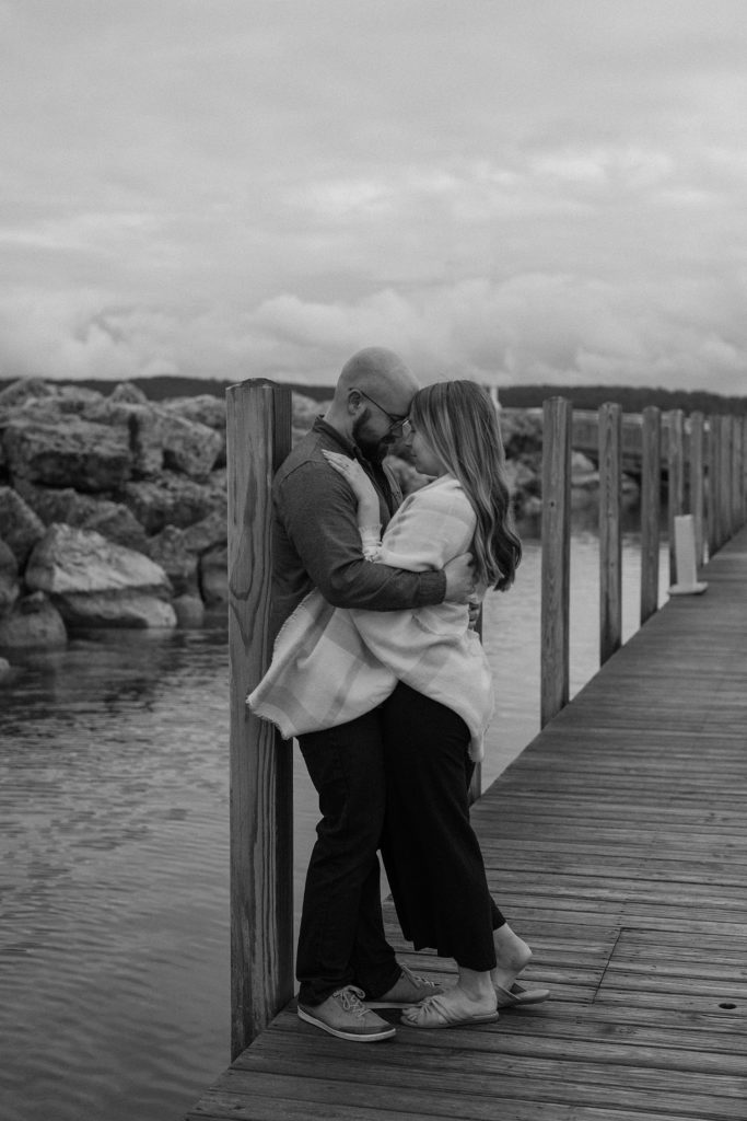 couple hugging while leaning against a post on a pier 