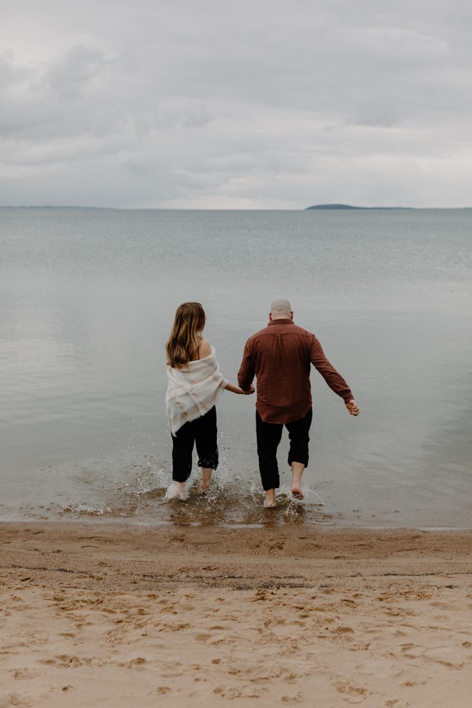 couple holding hands and walking in the water 