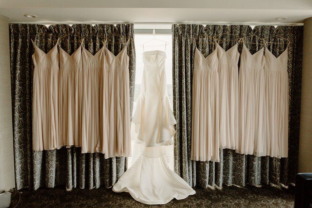 wedding dress handing in front of window with bridesmaids dresses next to it