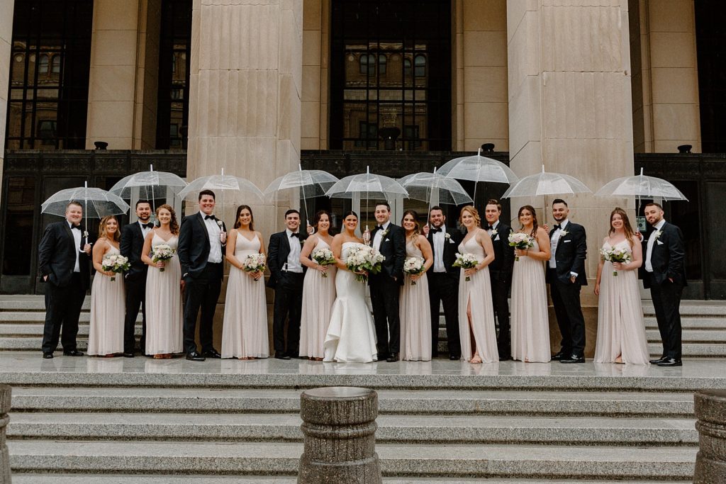 couple and wedding party standing on steps holding umbrellas 