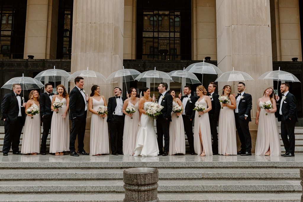 couple and wedding party standing outside laughing white it rains 