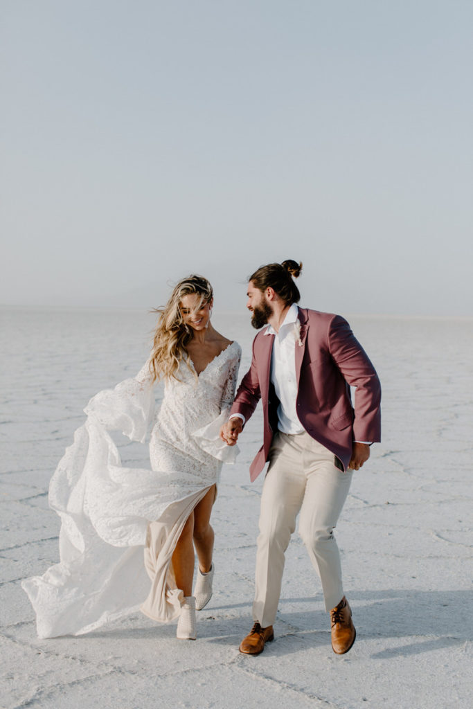 elopements vs weddings, groom holding brides hand and looking at her while walking on a salt flat