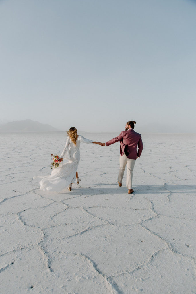 bride and groom holding hands walking along large white salt flats
