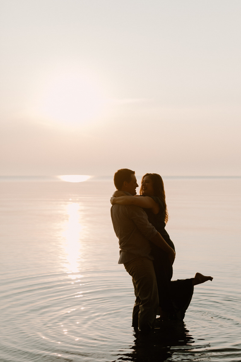 couple hugging each other while standing in the water at sunset