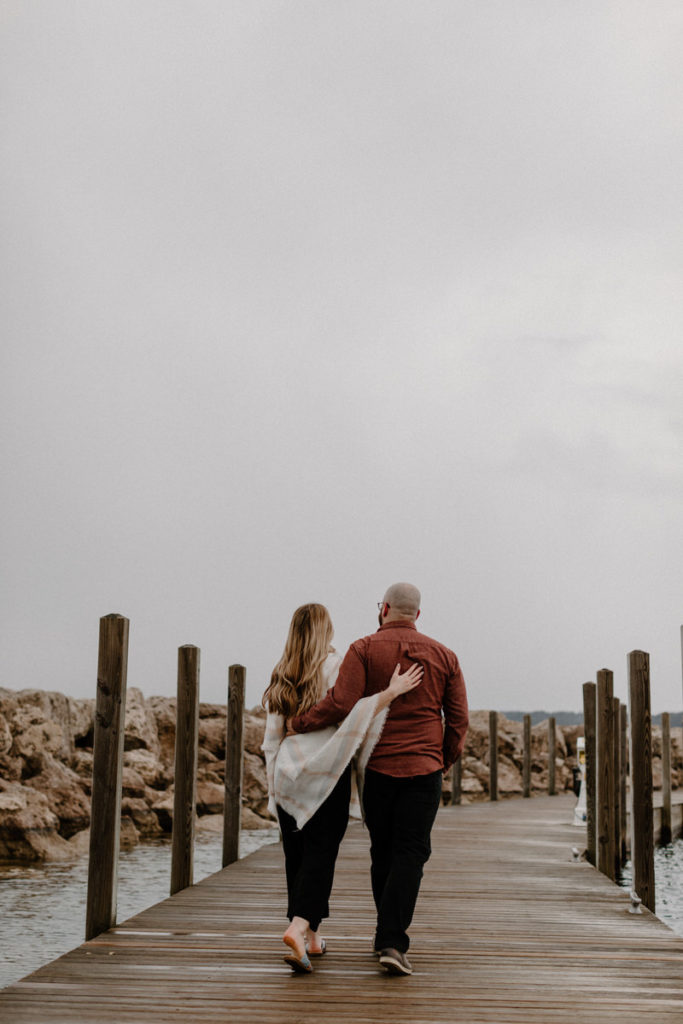 couple walking on pier with their arms around each other