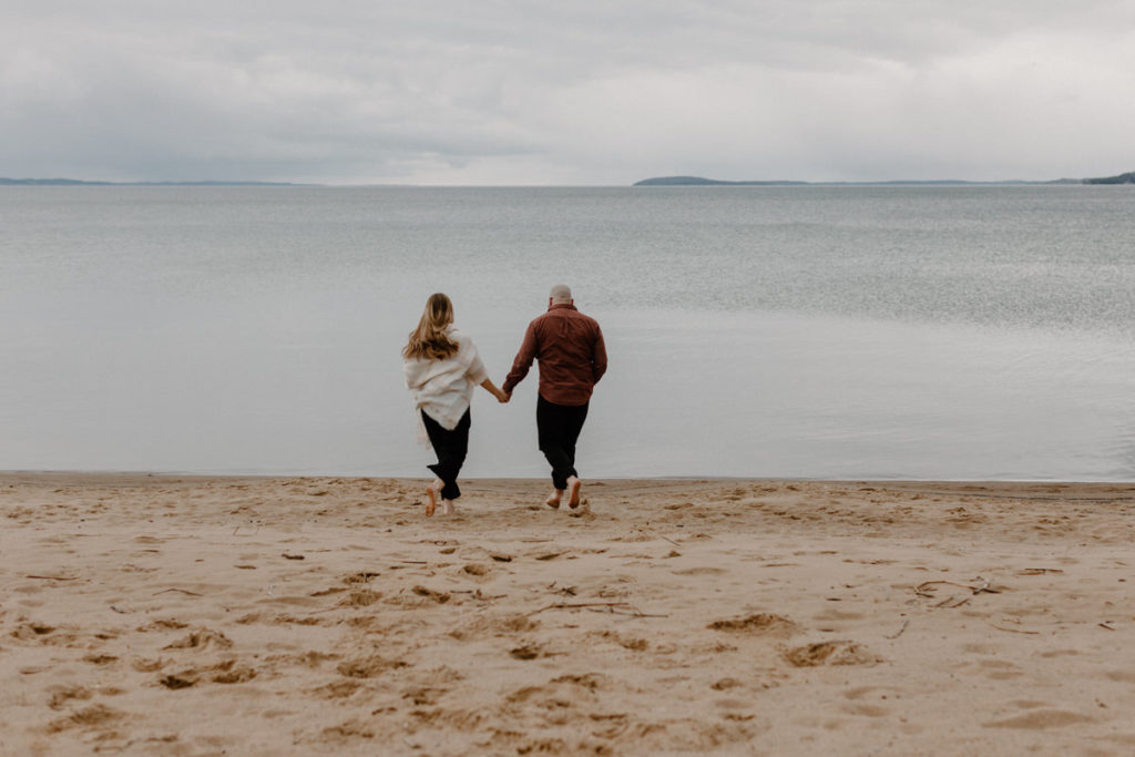 couple holding hands walking on the beach towards the water