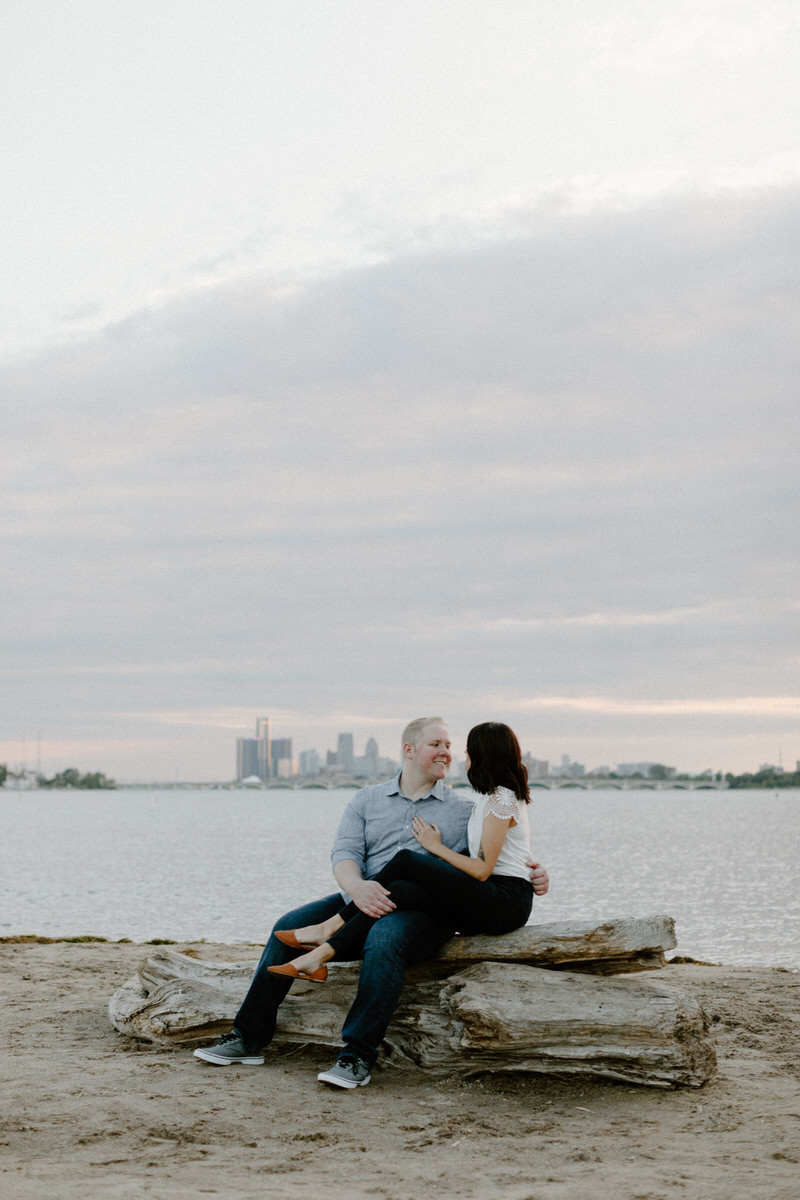 couple sitting on a rock next to each other looking at each other on the beach