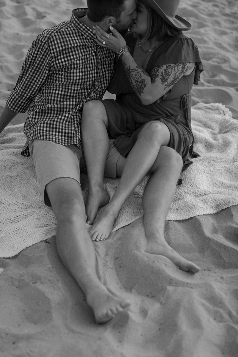 couple sitting on a blanket at the beach kissing