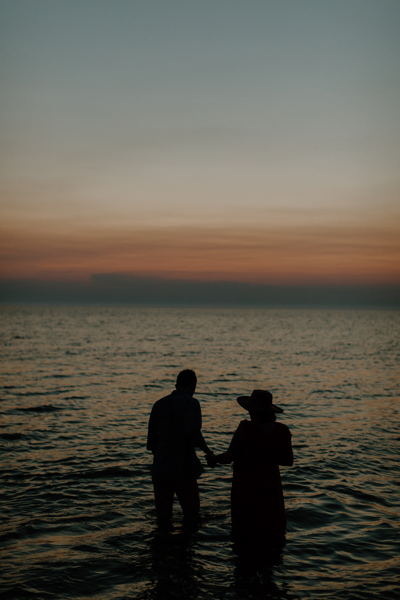 couple holding hands while standing in the water at sunset 