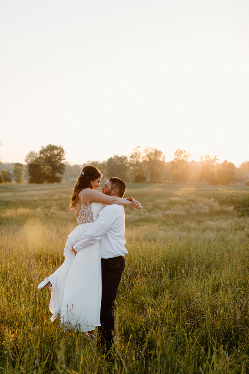 groom holding bride up in an open field 