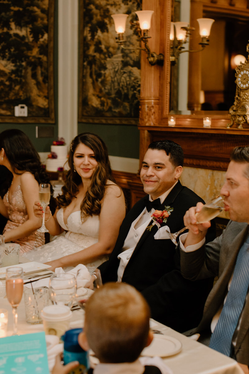 wedding couple sitting at reception table with guests