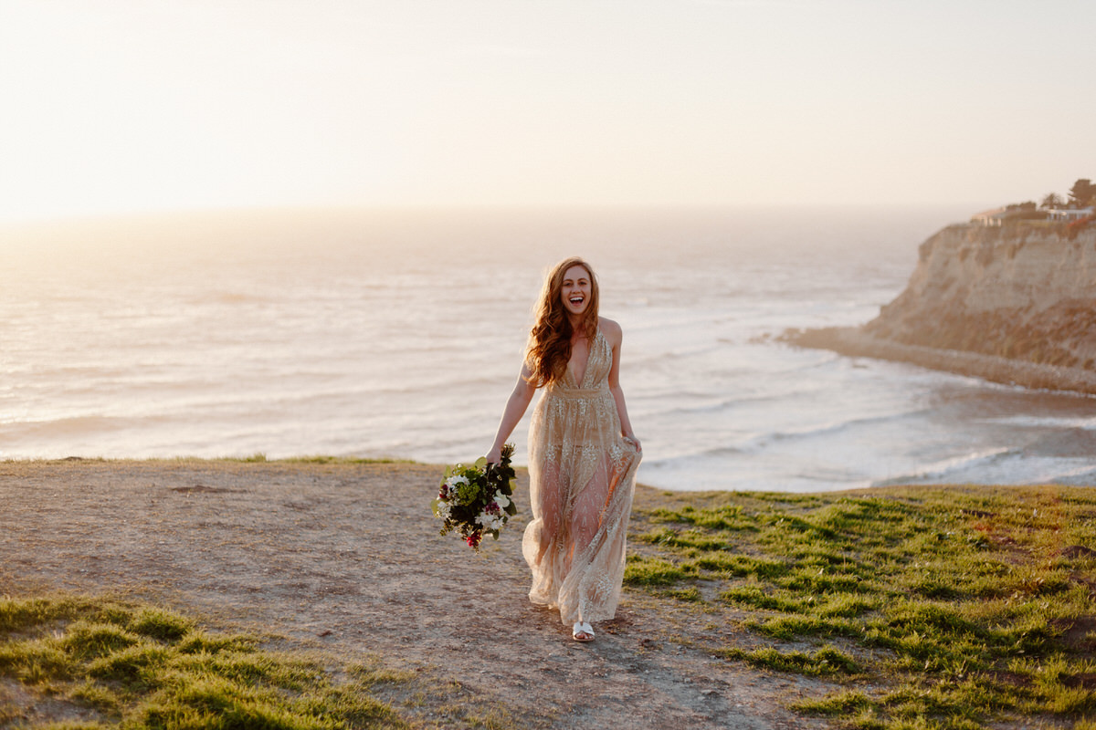 bride holding bouquet and walking along edge of oceanside cliff