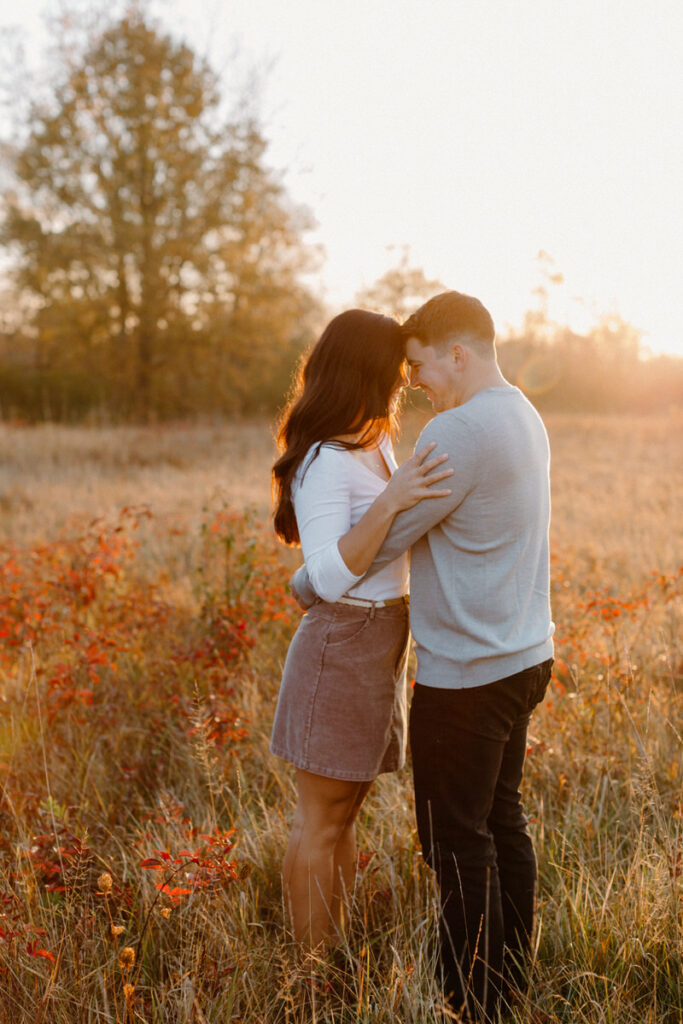 couple standing head to head with their arms around each other in a field