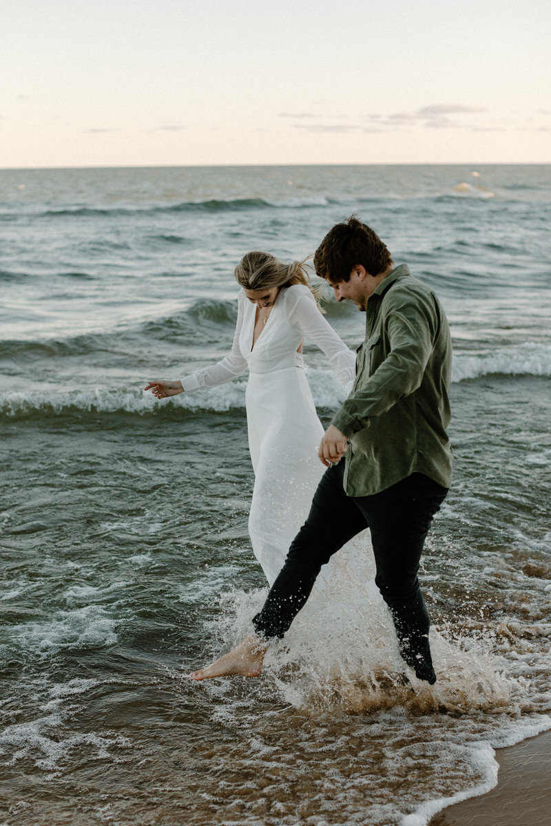 couple photoshoot outfit ideas featuring a couple kicking their feet in the shallow waves on the beach