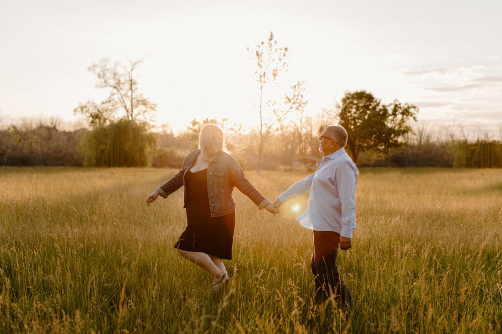 couple in a field at sunset holding hands as one of them skips 