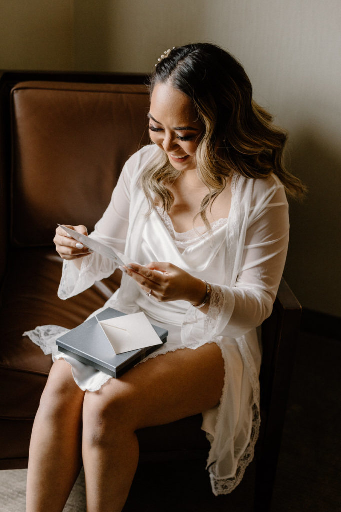 bride sitting in a chair reading a small card with a gift on her lap
