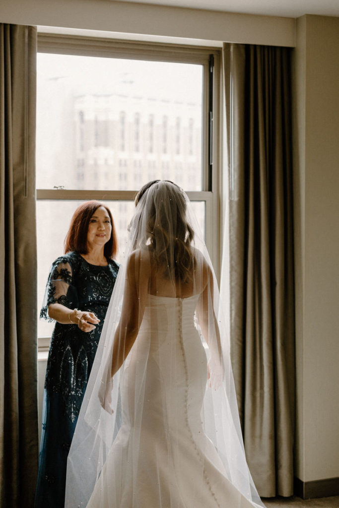 a mother standing in front of her daughter in a wedding dress smiling 