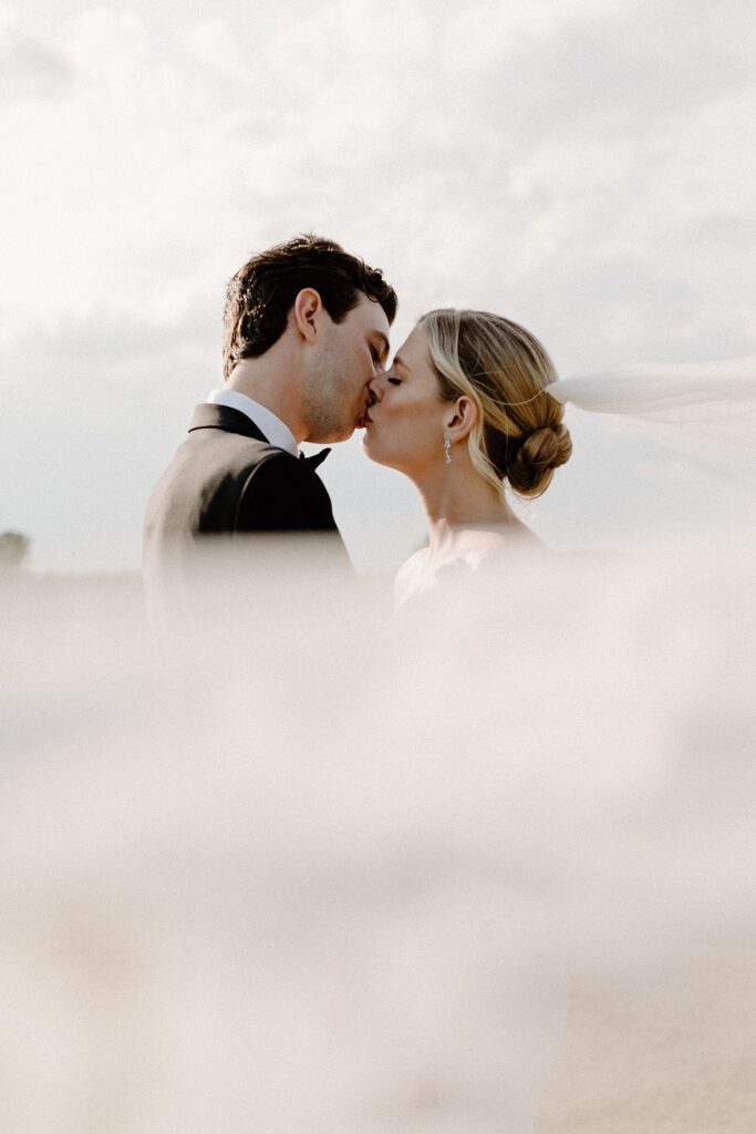 Wedding couple kissing while a vail is covering the bottom half of the image 