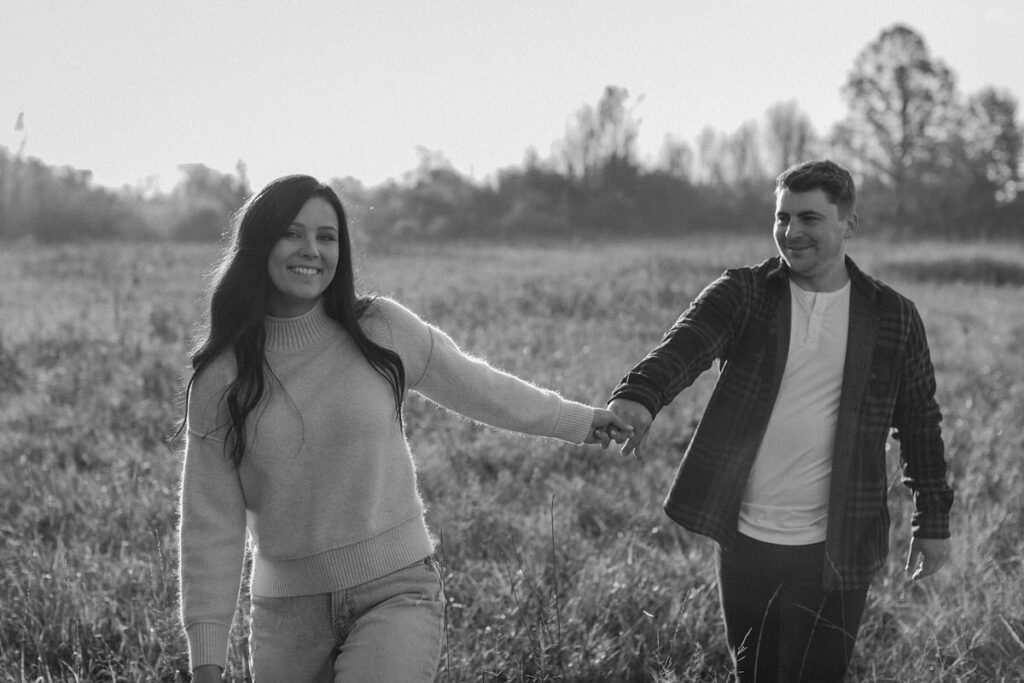 black and white photo of a couple holding hands while walking in a large field
