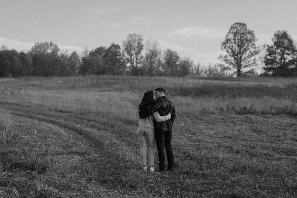 black and white photo of a couple with their arms around each other standing in a field