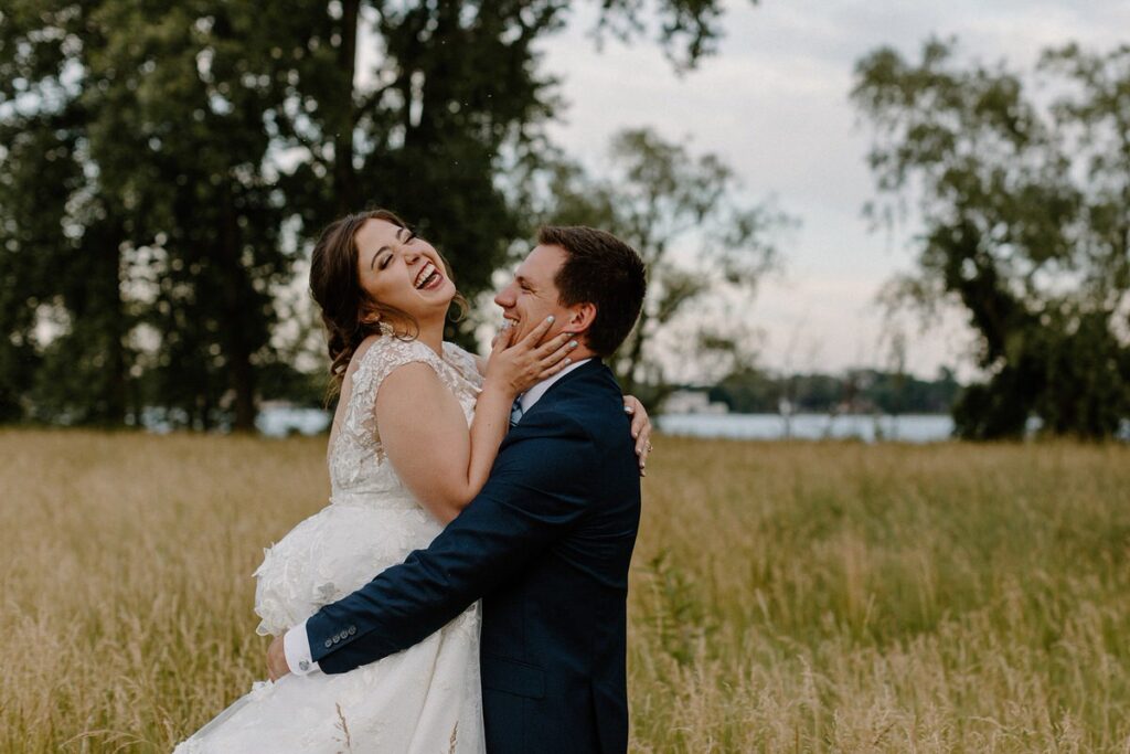 Man holding a woman up while they are standing in an open field on their wedding day 