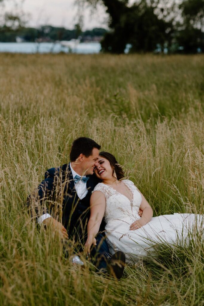 Bride and groom sitting in a field of tall grass together as they lean in for a kiss 