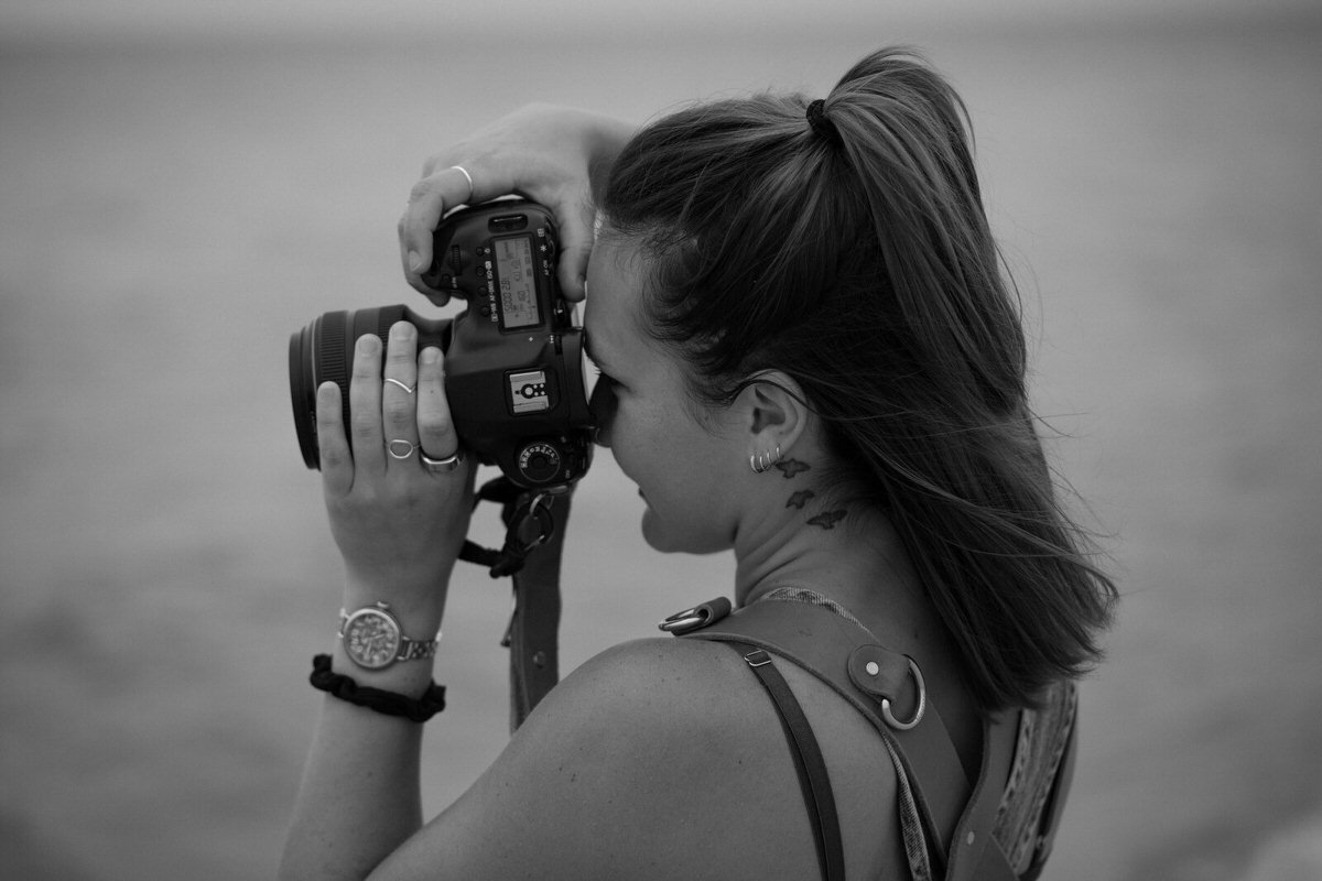 Featured image for how to become a full time photographer featuring a black and white photo of a photographer holding a camera up to her eye.
