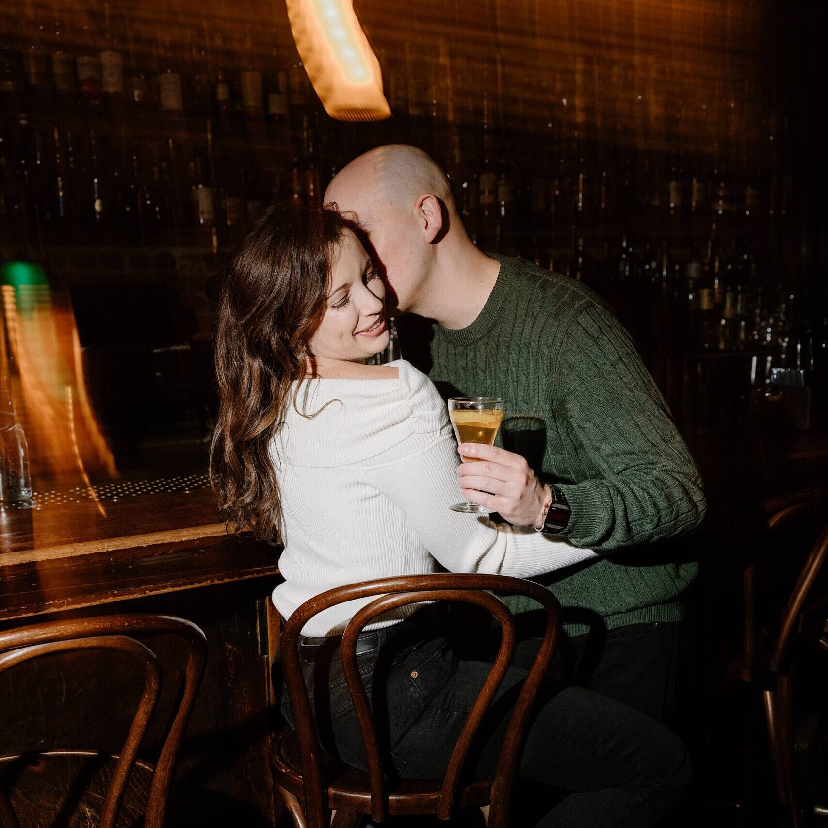 a couple embracing at a bar counter with a cocktail in hand